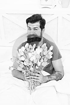 Make surprise concept. Gift for spouse. Bearded hipster in bed. Spring in bedroom. Man hold tulips bouquet while