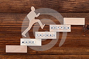 Make things better - Improvement Concept. Paper man climbing the steps to success in a conceptual image over wooden background