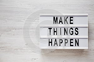 `Make things happen` words on a lightbox on a white wooden background, top view. Overhead, from above, flat lay. Copy space