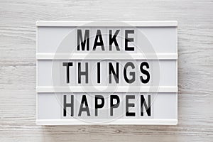 `Make things happen` words on a modern board on a white wooden background, top view. Overhead, from above, flat lay. Close-up