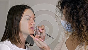 A make-up artist applies lipstick to the lips of a young woman with a special brush. Professional makeup.