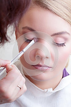 Make-up artist applying with brush color eyeshadow on female eye