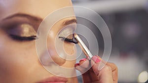 Make-up artist applying golden eye shadow makeup to the model`s eyes. Close up view