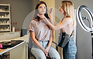A make-up artist is applying makeup to a woman client. Woman with blond hair doing makeup to a woman with brown hair