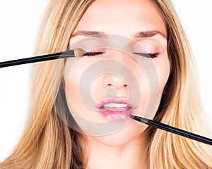 Make-up artist applying shadows and shine with cosmetic brushes. Close up.