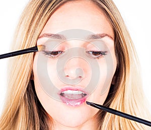 Make-up artist applying shadows and shine with cosmetic brushes. Close up.