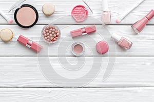 Make-up artist desk with powder, decorative cosmetics and macaroon cookies on white wooden background top view mokeup