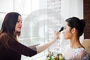 Make-up artist doing make up for young beautiful bride