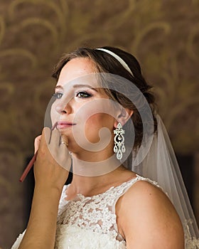 Make-up artist doing make up for young beautiful bride applying wedding make-up.