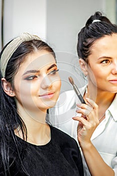 Make-up artist doing makeup for young beautiful bride applying wedding makeup in a beauty salon.