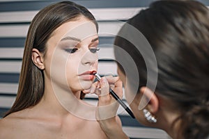 Make-up artist doing visage for beautiful teenage girl, using lipstick for lips. Make up, cosmetics, beauty standards, skin care