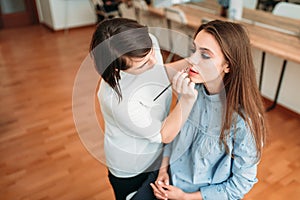 Make up artist hand applying gloss on woman lips