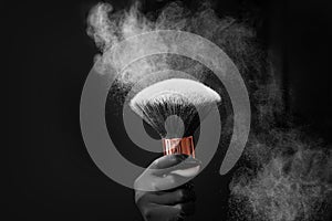 Make-up artist holds brush for white powder with dust on black background