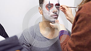 Make-up artist makes greasepaint on man`s face before his performance on scene