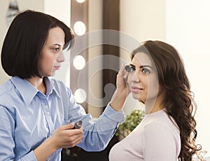 Make-up artist makes up eyelashes for beautiful girl photo