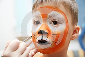 Make up artist making tiger mask for child.Children face painting. Boy painted as tiger or ferocious lion