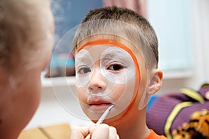 Make up artist making tiger mask for child. Children face painting. Boy painted as tiger or ferocious lion. Preparing for theatre