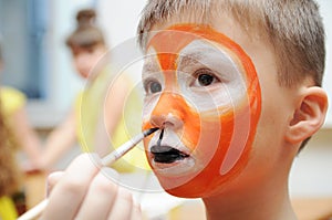 Make up artist making tiger mask for child.Children face painting. Boy painted as tiger or ferocious lion. Preparing