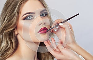 The make-up artist paints the lips of a beautiful woman, completes make-up in the beauty salon.