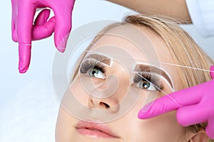 The make-up artist plucks eyebrows with a thread close-up. Woman Having Permanent Makeup Tattoo on her Eyebrows. Professional