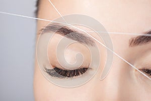 The make-up artist plucks eyebrows with a thread close-up. Women`s cosmetology in the beauty salon