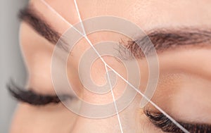 The make-up artist plucks eyebrows with a thread close-up. Women`s cosmetology in the beauty salon