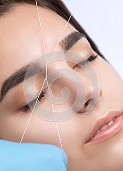 The make-up artist plucks eyebrows with a thread close-up. Women`s cosmetology in the beauty salon