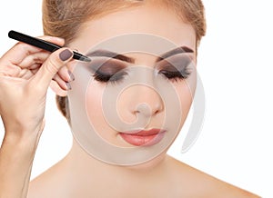 Make-up artist plucks eyebrows with tweezers to a woman with smoky eyes makeup. Beautiful thick eyebrows close up. Professional