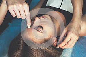 The make-up artist plucks her eyebrows with a thread of a beautiful brunette in a beauty salon.