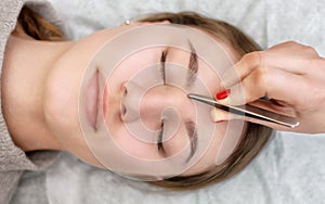 The make-up artist plucks her eyebrows from a young woman in a beauty salon. photo