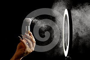 Make-up artist`s hand with makeup brushes in front of a ring lamp against