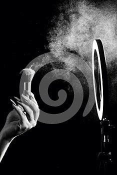 Make-up artist`s hand with makeup brushes in front of a ring lamp against. Black and white photo