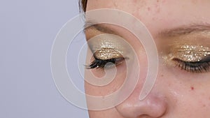 Make-up artist sticks long black false eyelashes on the eyes of a young beautiful girl model with bright evening gold