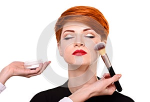 Make-up artist working with brush on model face. Beautiful young woman with short red hair.