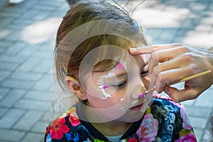 A make-up artist works over the face of a little girl. Child creativity. The master paints a beautiful figure on the face of a