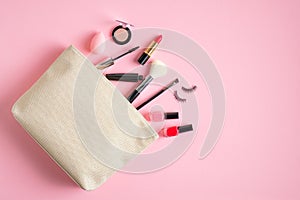 Make up bag with cosmetic beauty products spilling out on pink background. Flat lay, top view