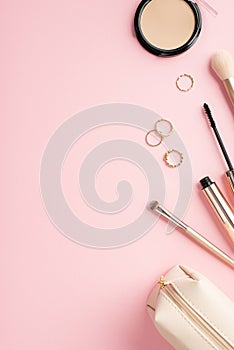 Make up beauty concept. Top view vertical photo of gold rings compact powder makeup brushes mascara and cosmetic bag on pastel