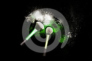 Make-up brush with colorful powder on black background. Explosion stars dust with bright colors. White and green powder.