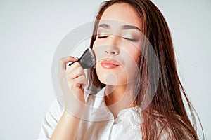 Make up brush kabuki in hand of smiling asian young woman with dark long hair on white background