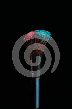 Make-up brush with pink and blue powder isolated on black background