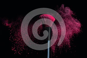 Make-up brush with pink powder explosion isolated on a black background