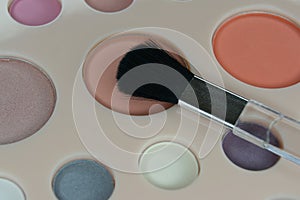 The make up brush is placed on the eye shadow palette. Close up.