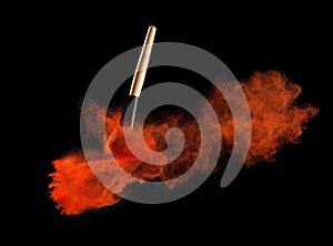 Make-up brush with redpowder explosion on black background
