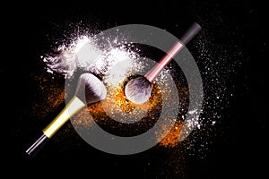 Make-up brushes with colorful powder on black background. Explosion stars dust with bright colors. White and orange powder.