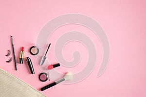 Make-up cosmetic bag with beauty products spilling out on to pastel pink background. Flat lay, view from above