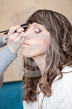 Make-up designer hand with brush applying cosmetic on woman face with curly hair