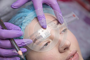 Make-up for eyebrows of beautiful woman with thick brows in beauty salon. Closeup beautician doing tattooing eyebrow.