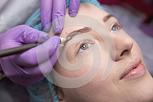 Make-up for eyebrows of beautiful woman with thick brows in beauty salon. Closeup beautician doing tattooing eyebrow.