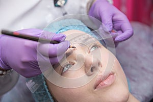 Make-up for eyebrows of beautiful woman with thick brows in beauty salon. Closeup beautician doing tattooing eyebrow.