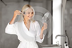 Daily Make Up. Portrait Of Beautiful Senior Woman Applying Blush In Bathroom